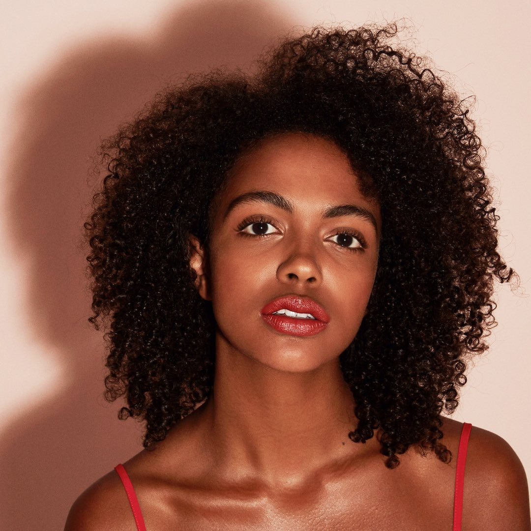 Woman with curly hair wearing makeup against a pink background