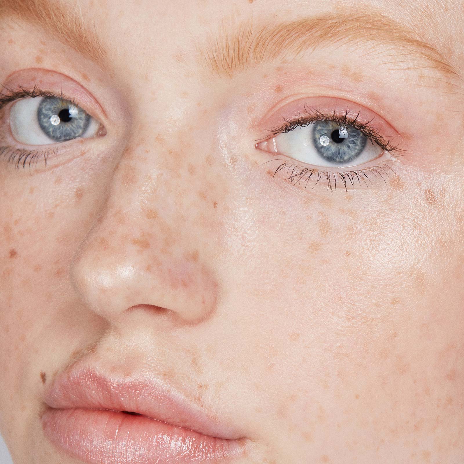 Close-up of a person's face wearing makeup with freckles and blue eyes.