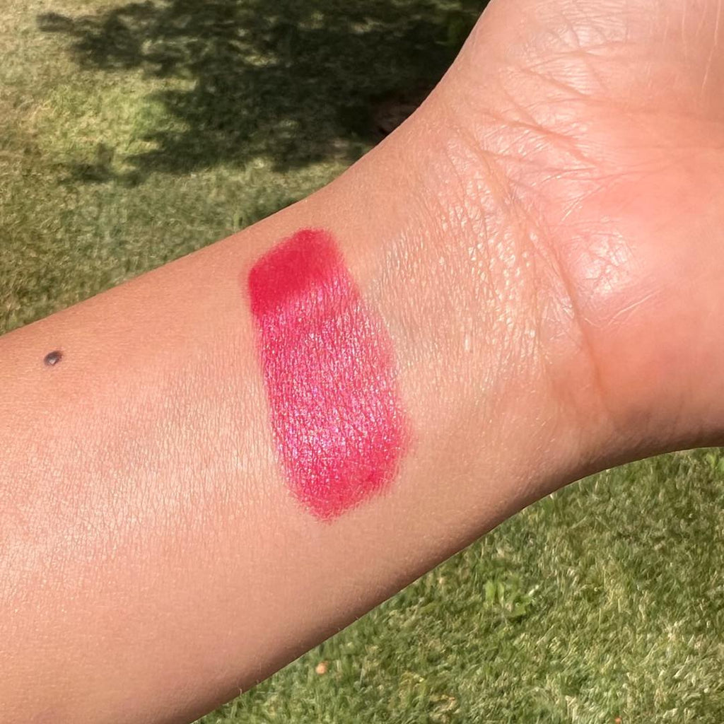 Pink lipstick swatch on a person's arm with a grassy background