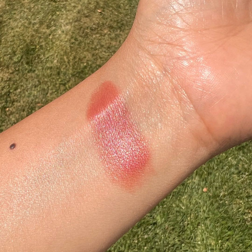 Close-up of a swatch of pink lipstick on a person's wrist with a grassy background