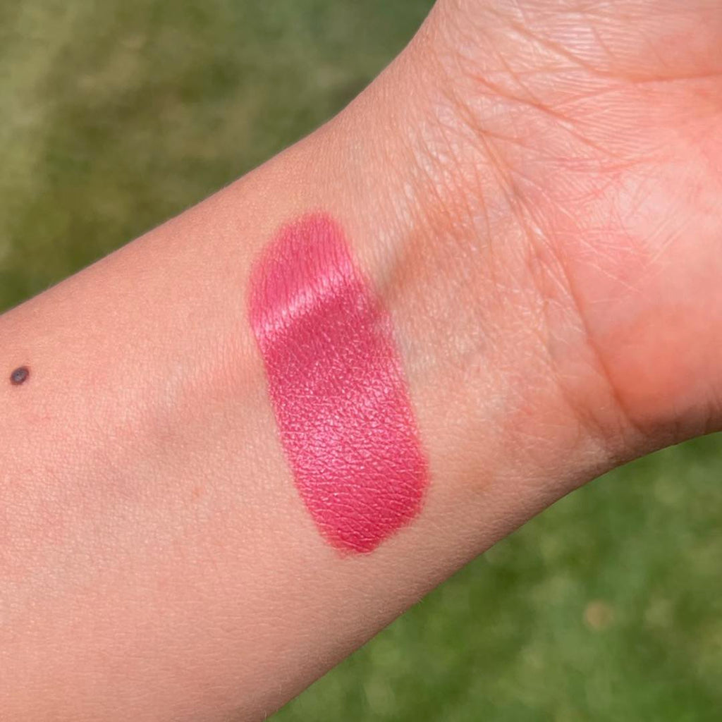 Pink lipstick swatch on a person's arm with a green outdoor background