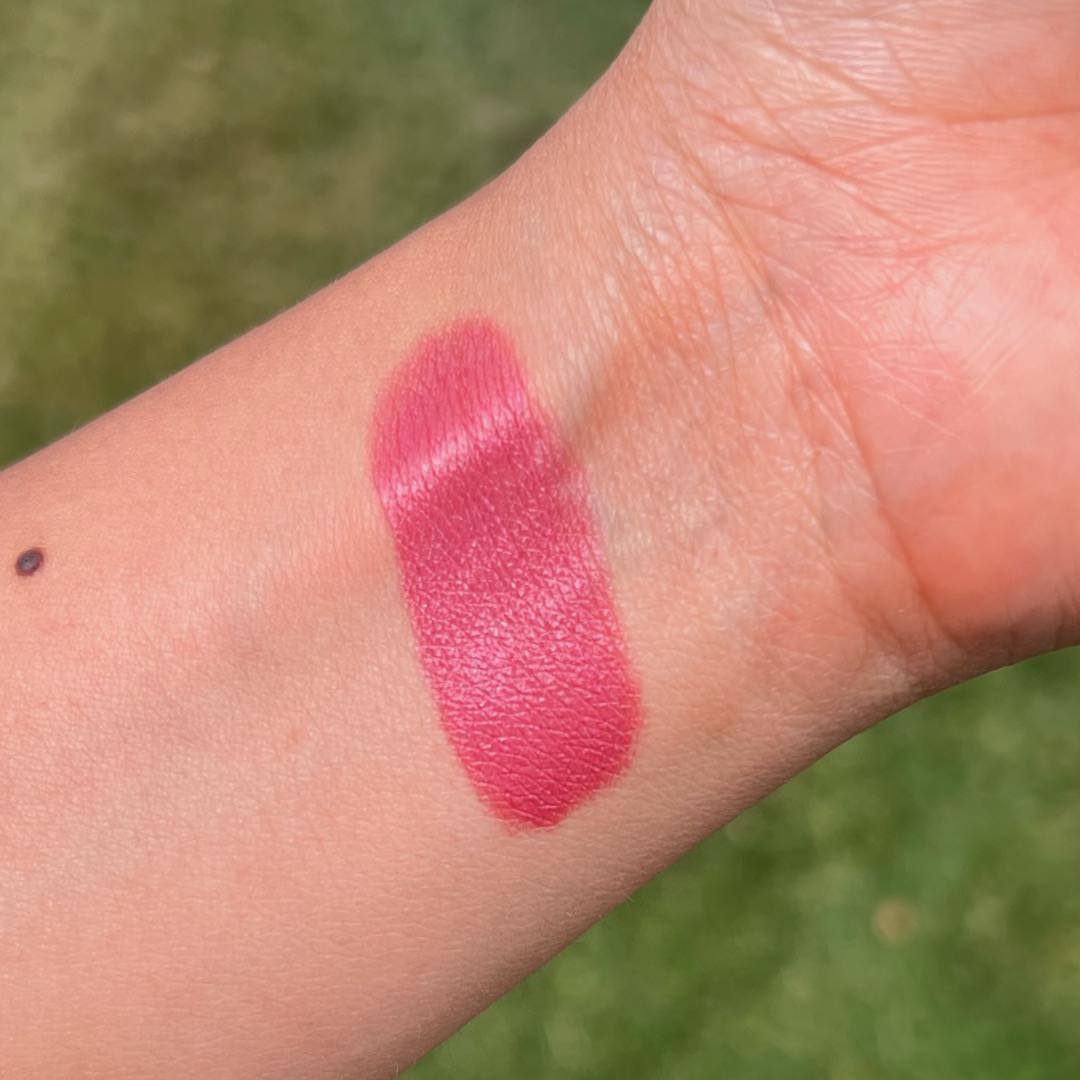 Pink lipstick swatch on a person's arm with a green outdoor background