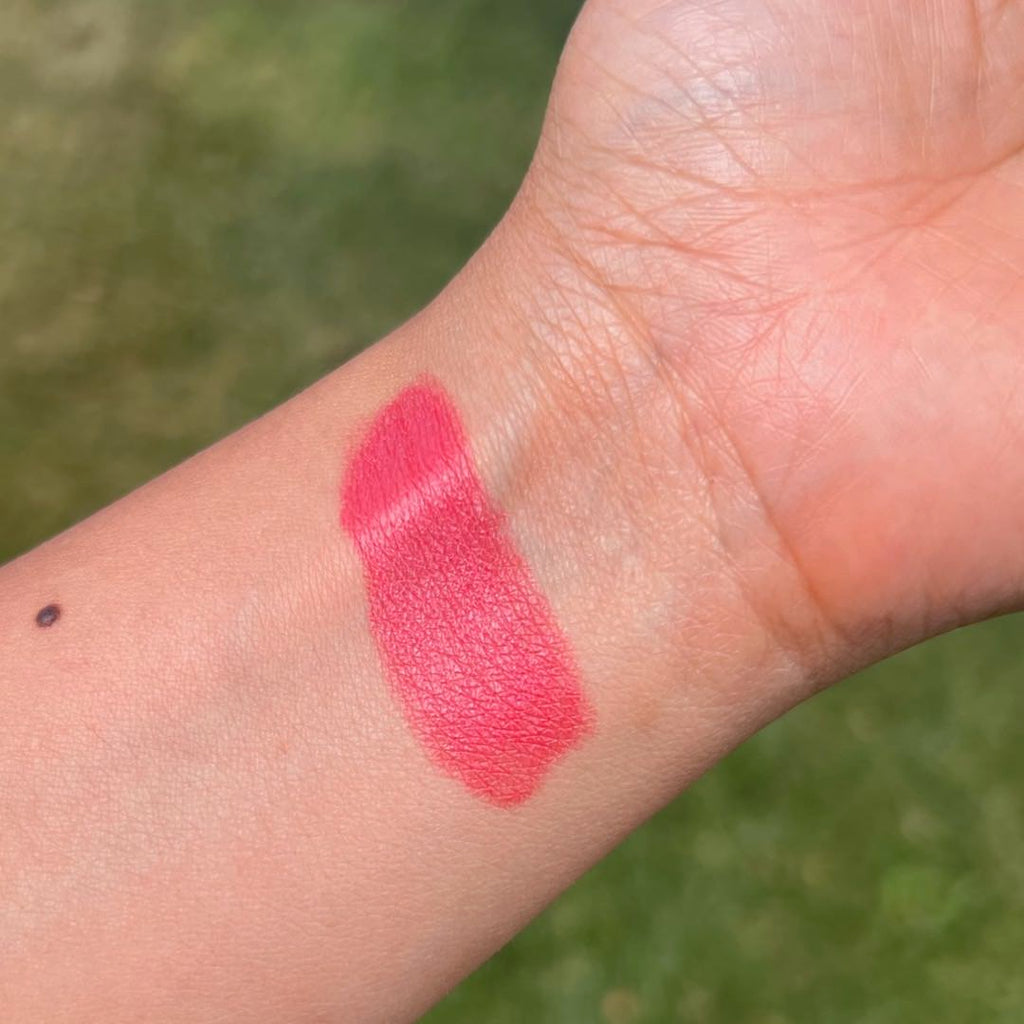 Pink lipstick swatch on a person's arm with a blurred green background