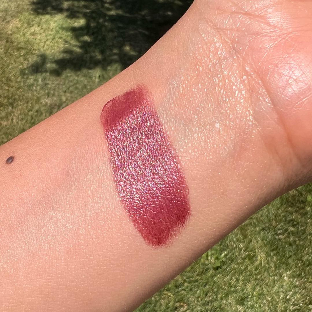 Wine colored lipstick swatch on a person's arm with a grassy background