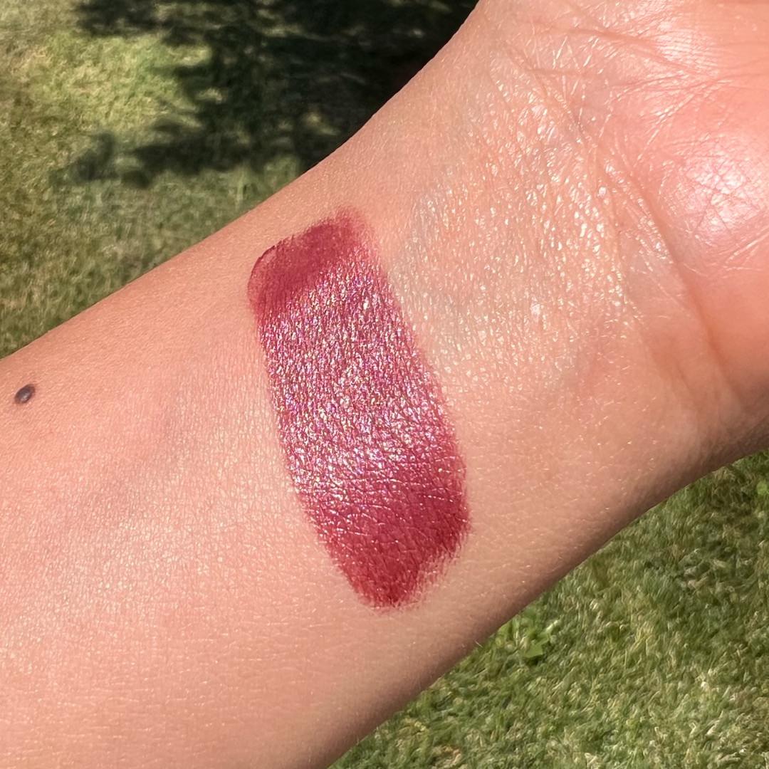 Wine colored lipstick swatch on a person's arm with a grassy background
