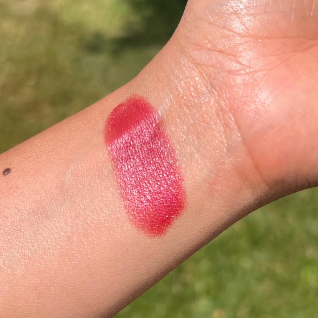 Close-up of a red lipstick swatch on a person's wrist with a blurred green background