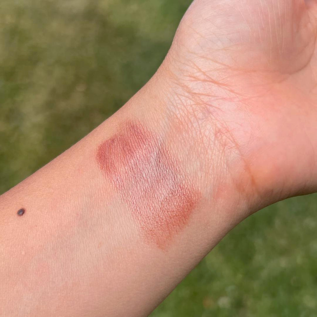 Makeup swatch on a person's arm with a blurred green background