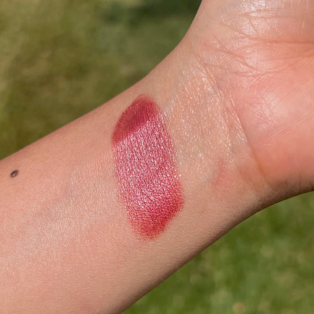 Red lipstick swatch on a person's arm with a blurred green background