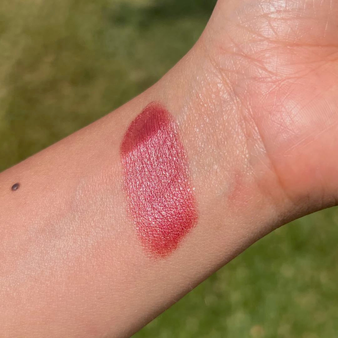 Red lipstick swatch on a person's arm with a blurred green background