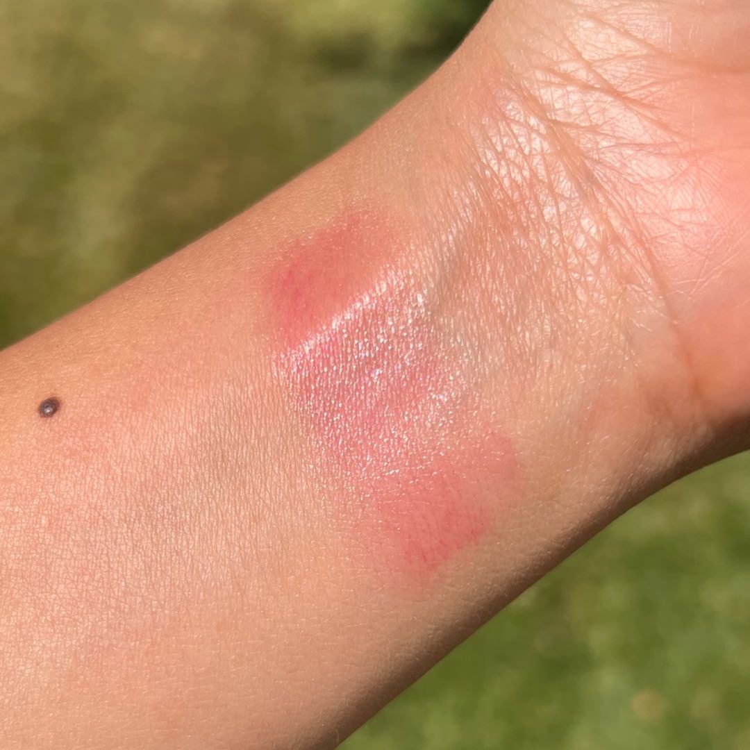 Close-up of a person's arm with a pinkish-red makeup swatch on a blurred green background