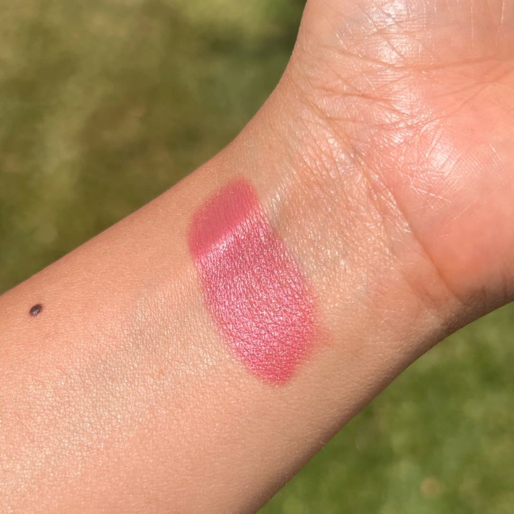 Pink lipstick swatch on a person's arm with a blurred green background