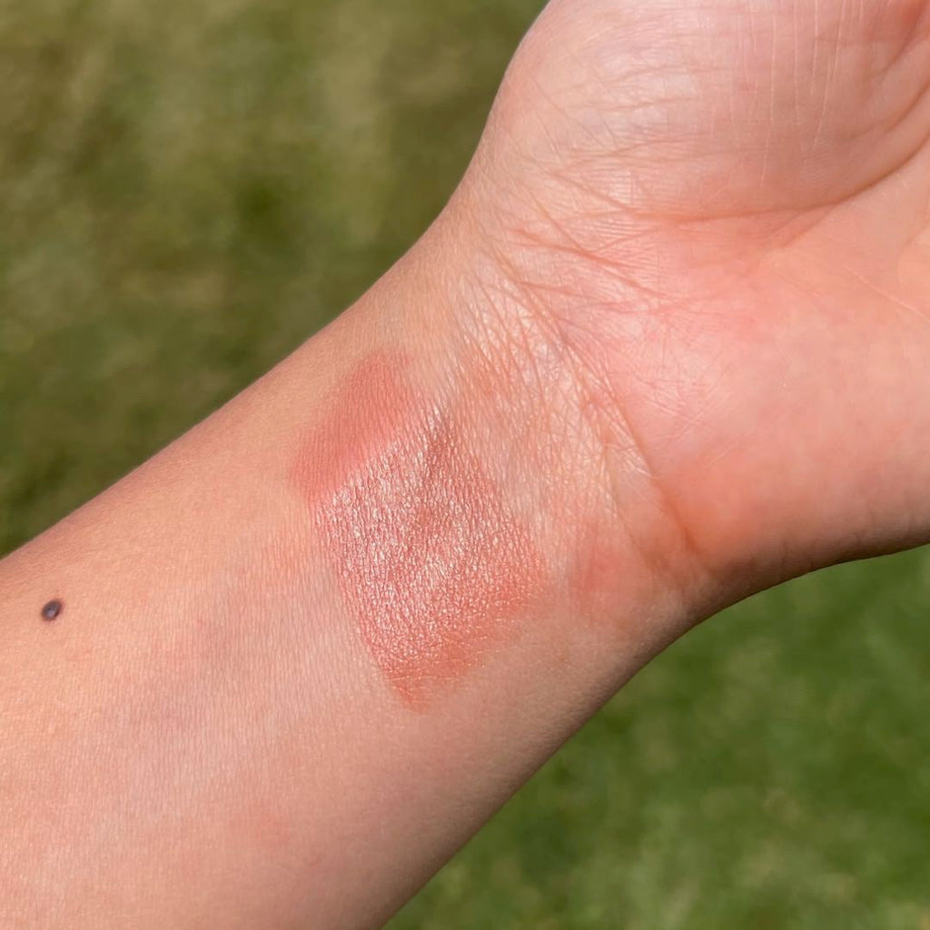 Close-up of a hand with a swatch of pink makeup on a green background