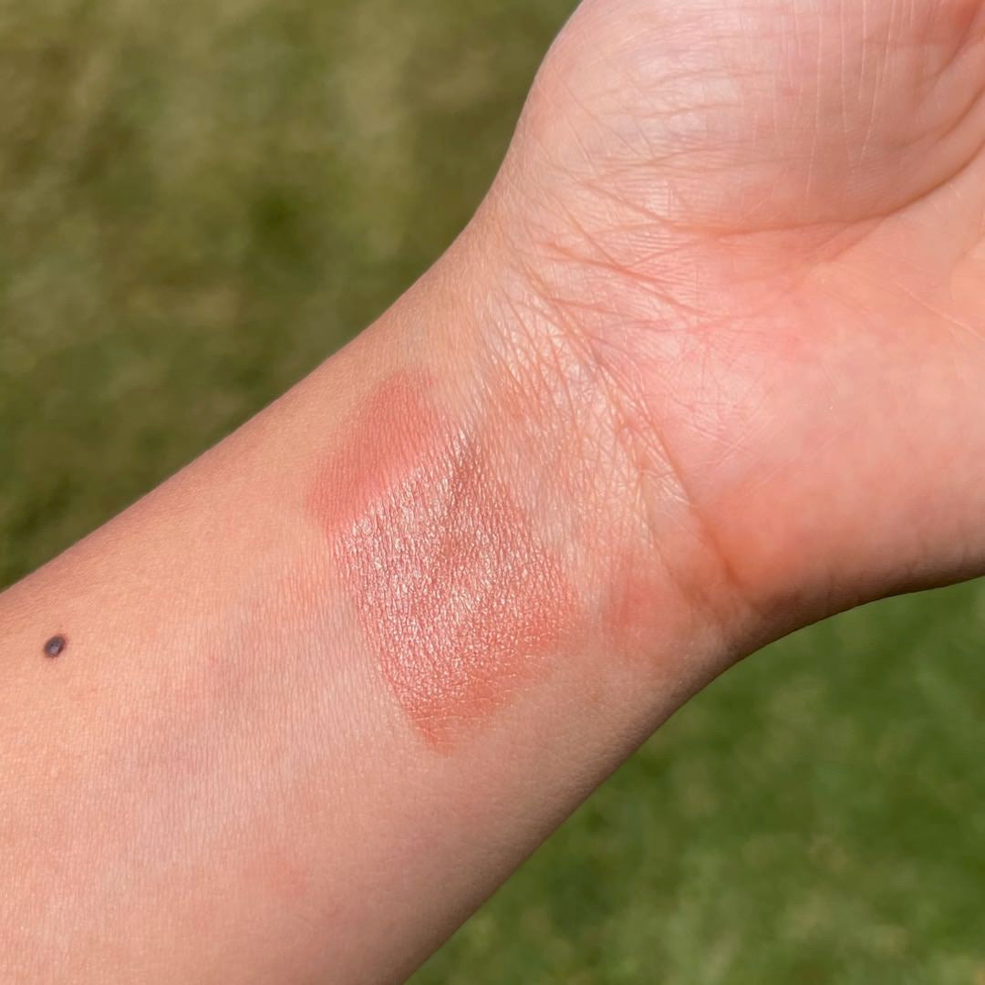 Close-up of a hand with a swatch of pink makeup on a green background