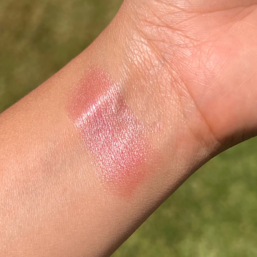 Close-up of a pinkish-brown color swatch on skin with a blurred green background