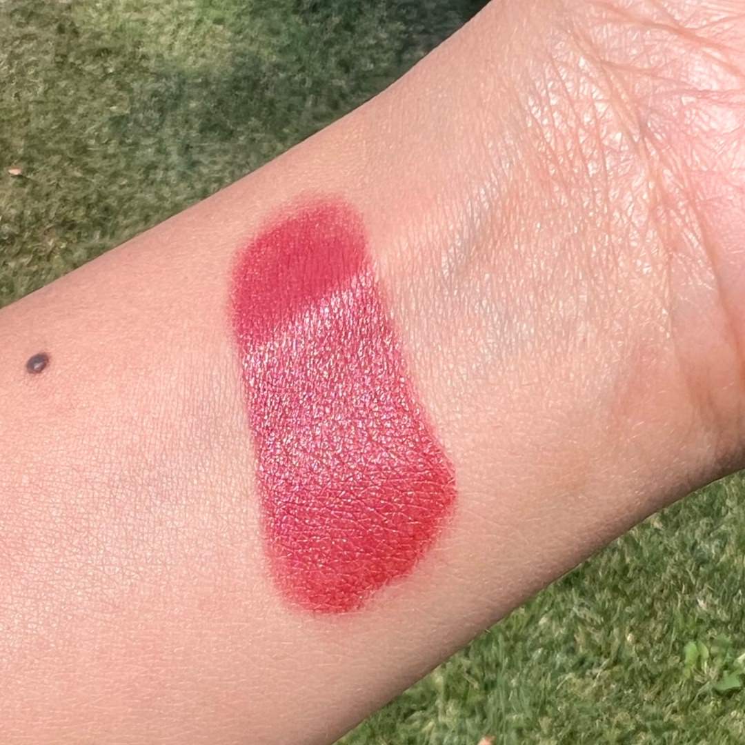 Red lipstick swatch on a person's arm with grass in the background