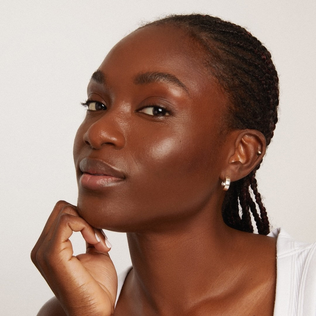 Woman wearing brown foundation makeup with braided hair against a plain background