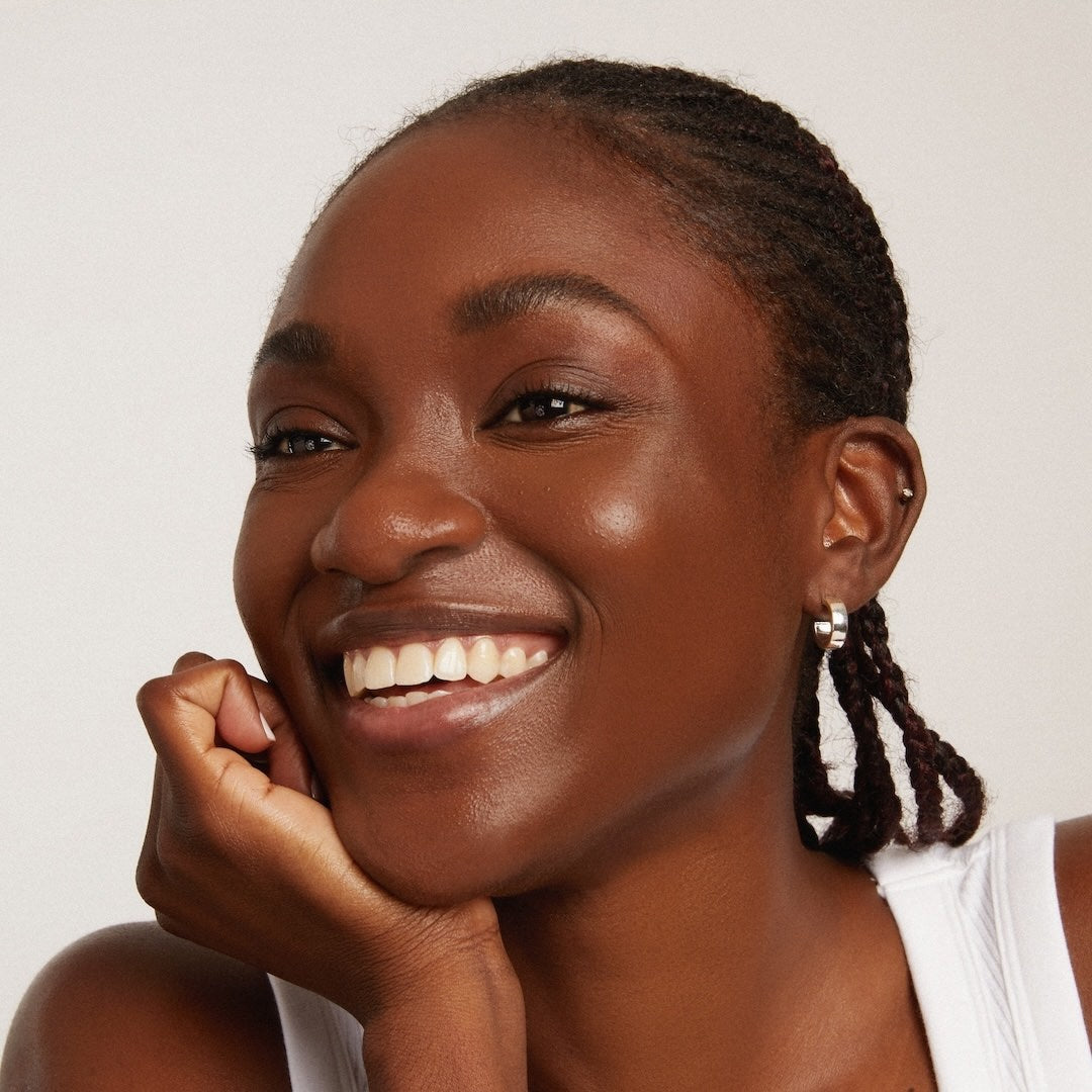 Woman wearing foundation makeup with braided hair smiling against a plain background