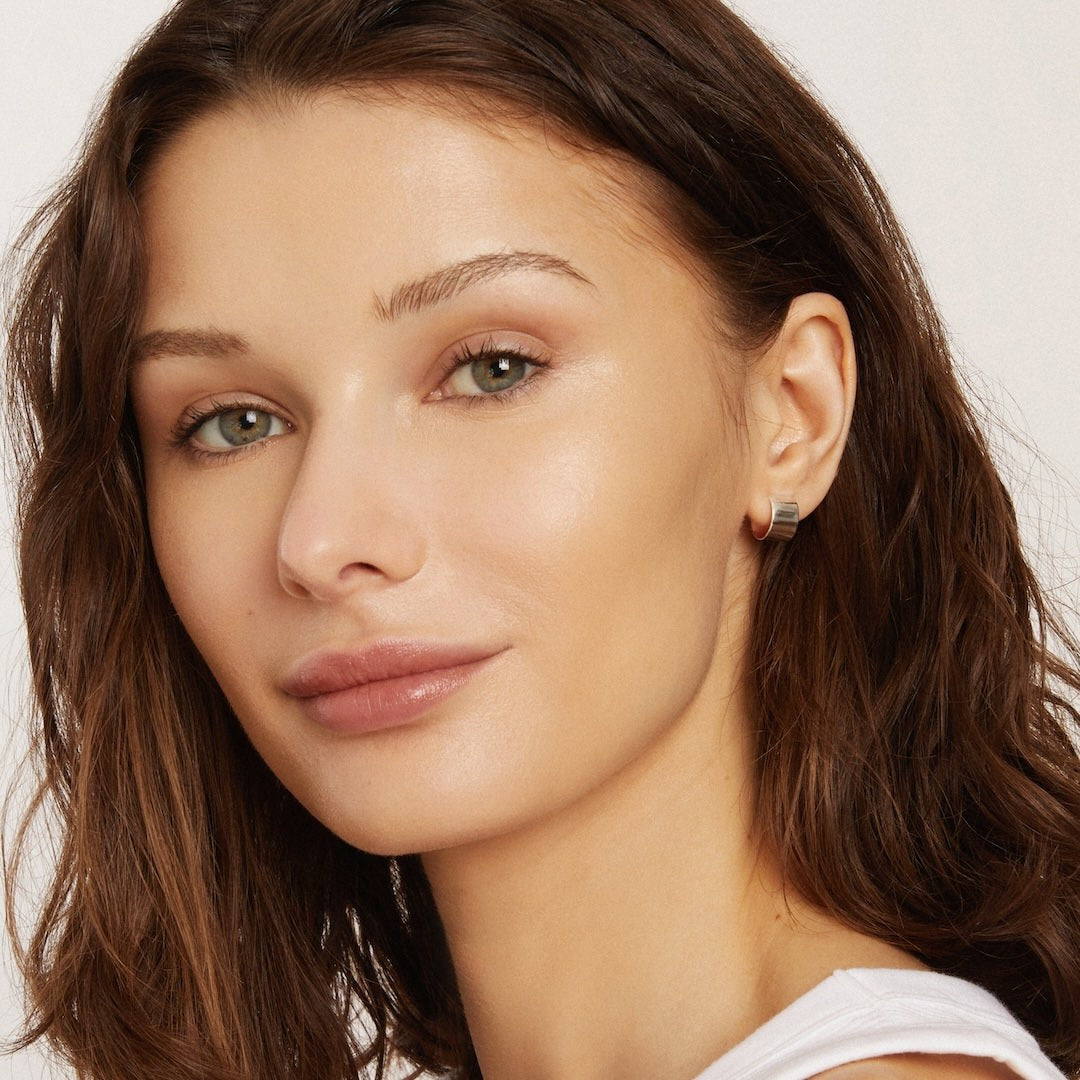 Close-up of a woman with a neutral expression wearing foundation makeup on a plain background