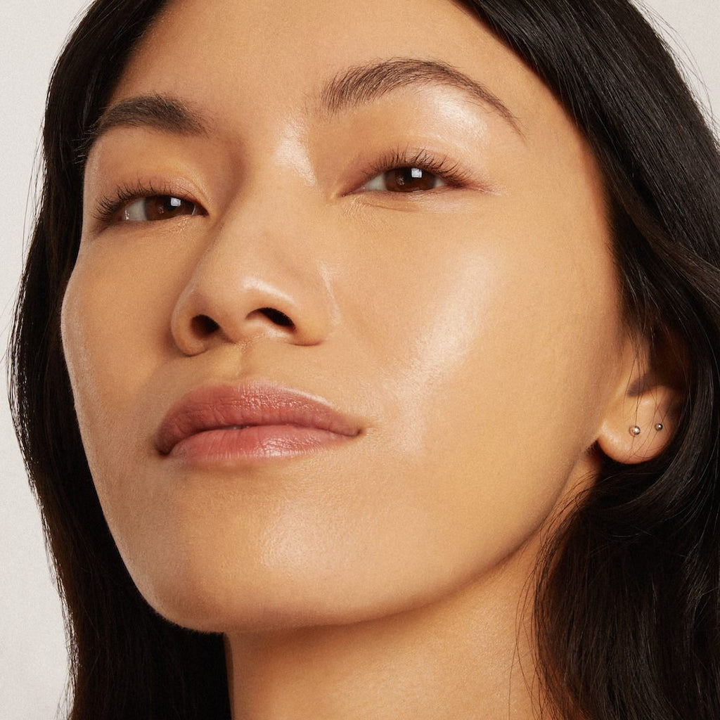 Close-up of a woman's face with a neutral expression wearing foundation makeup on a light background