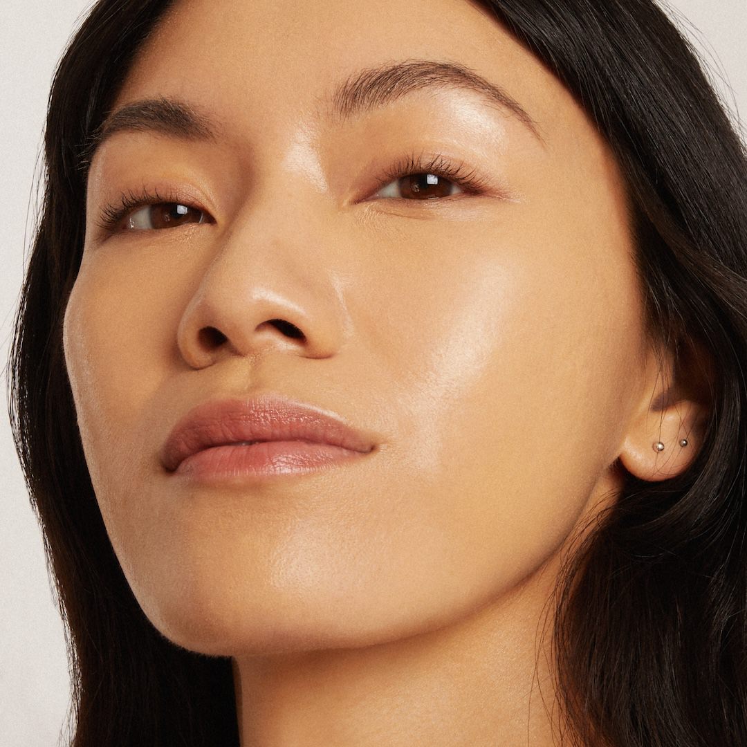Close-up of a woman's face with a neutral expression wearing foundation makeup on a light background