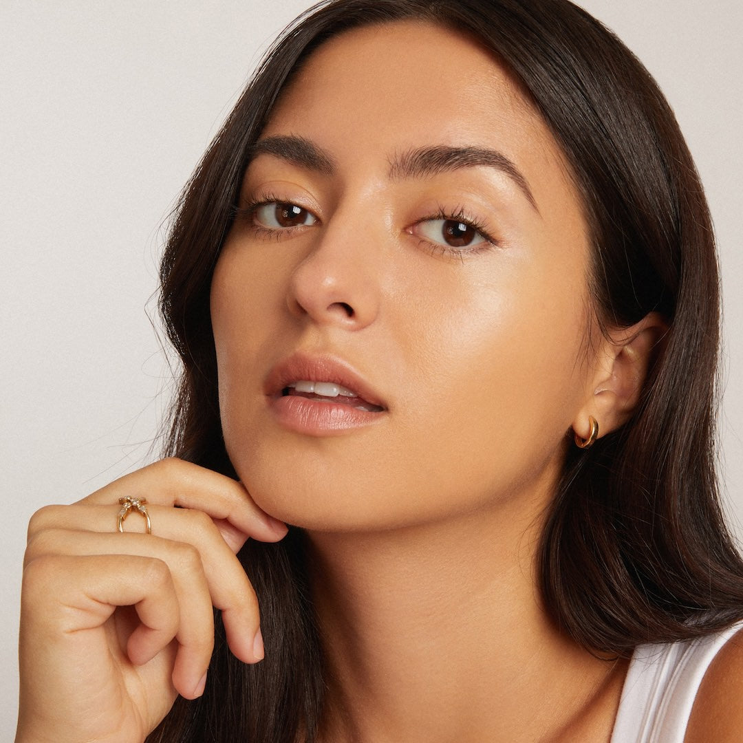 Close-up of a woman with a neutral expression wearing foundation makeup on a plain background