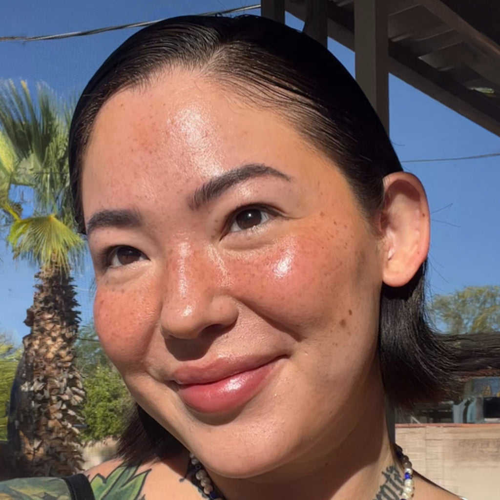 Woman with tattoos on her shoulder against a palm tree and clear blue sky background