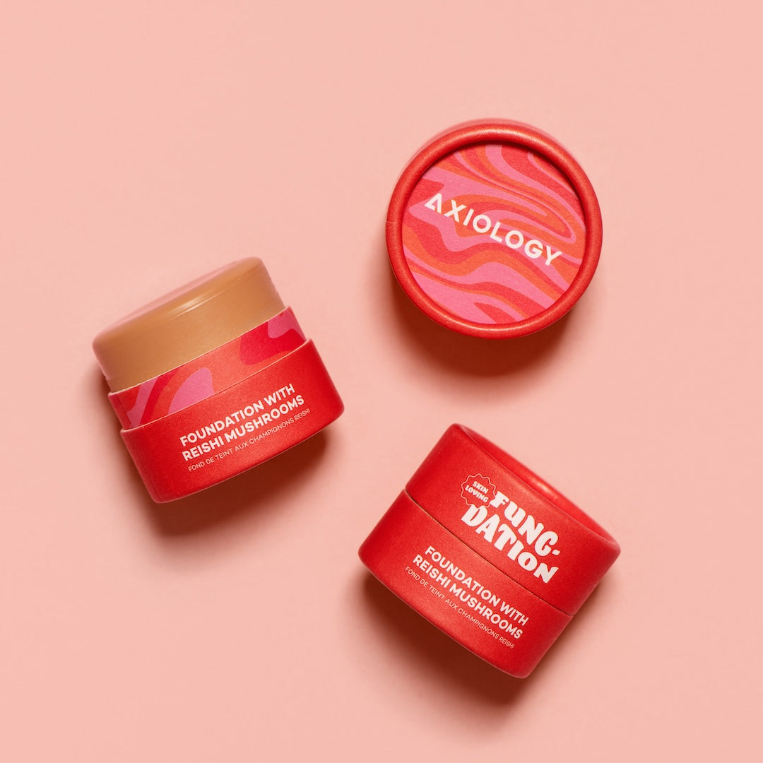Three red pots of Axiology foundation on a pink background