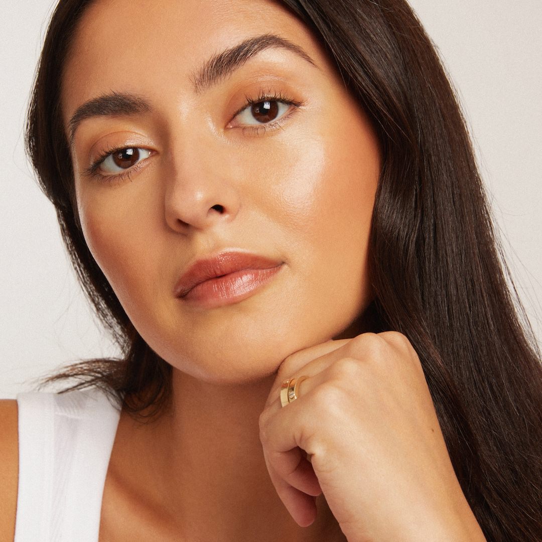 Close-up of a woman wearing makeup with a neutral expression on a plain background