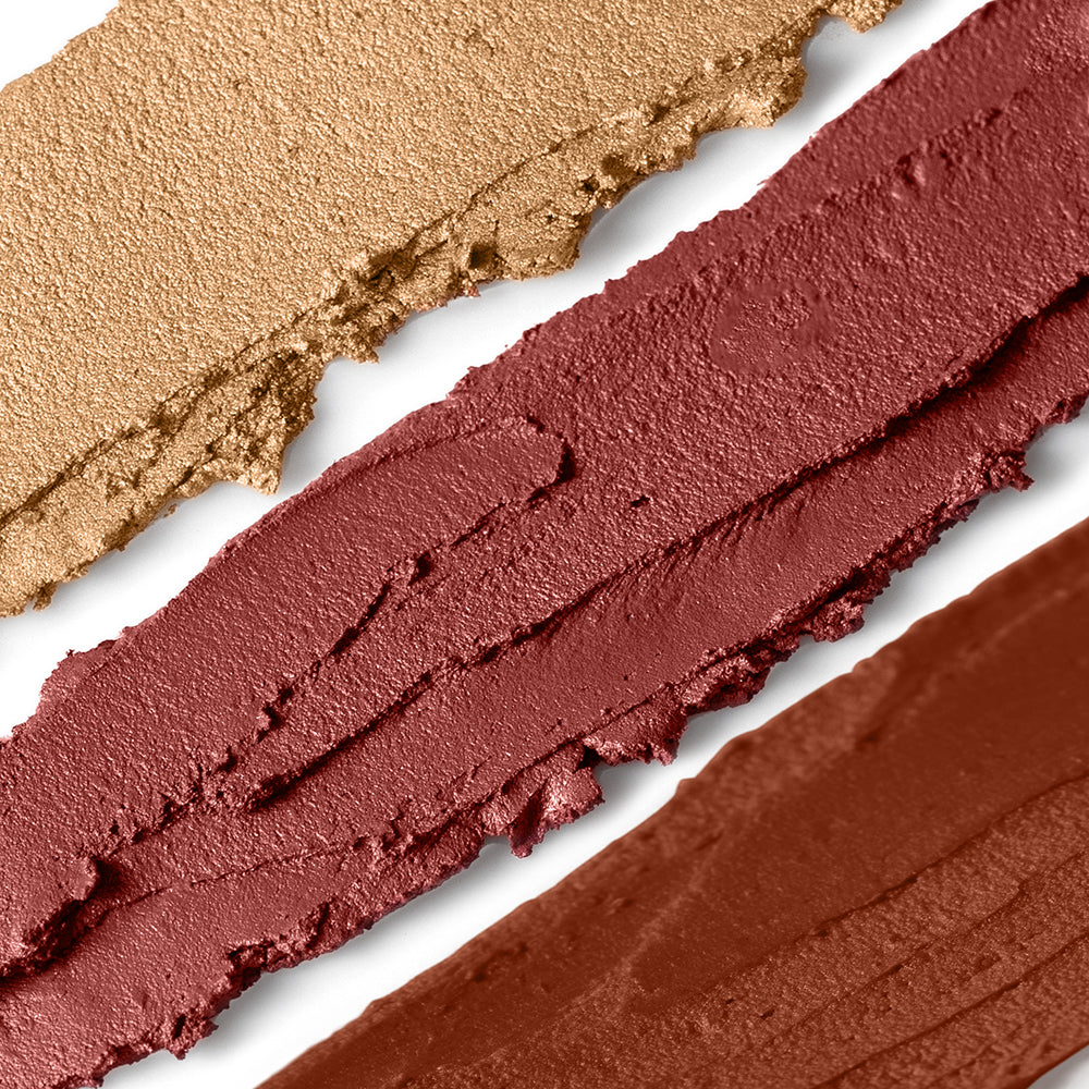 Close-up of three swatches of different red-brown makeup shades on a white background