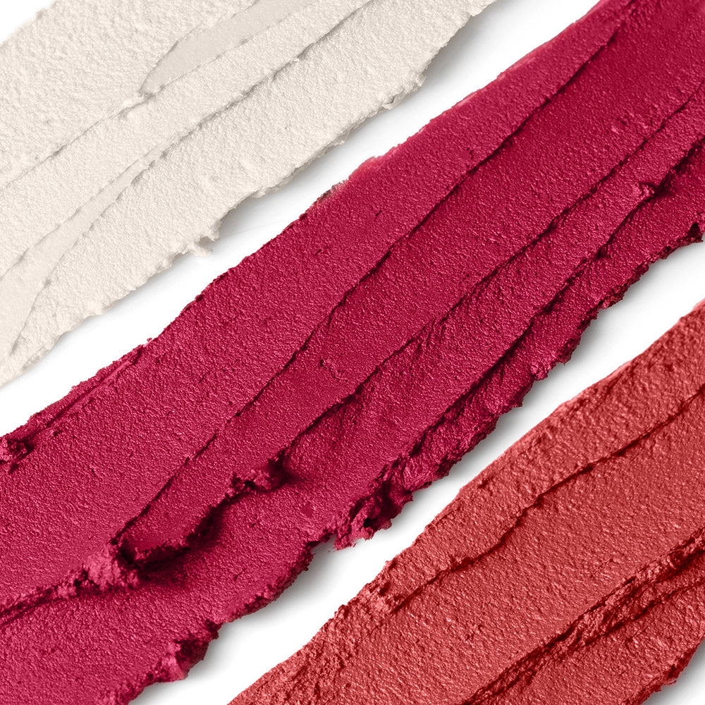 Close-up of three swatches of pink and red cosmetics on a white background