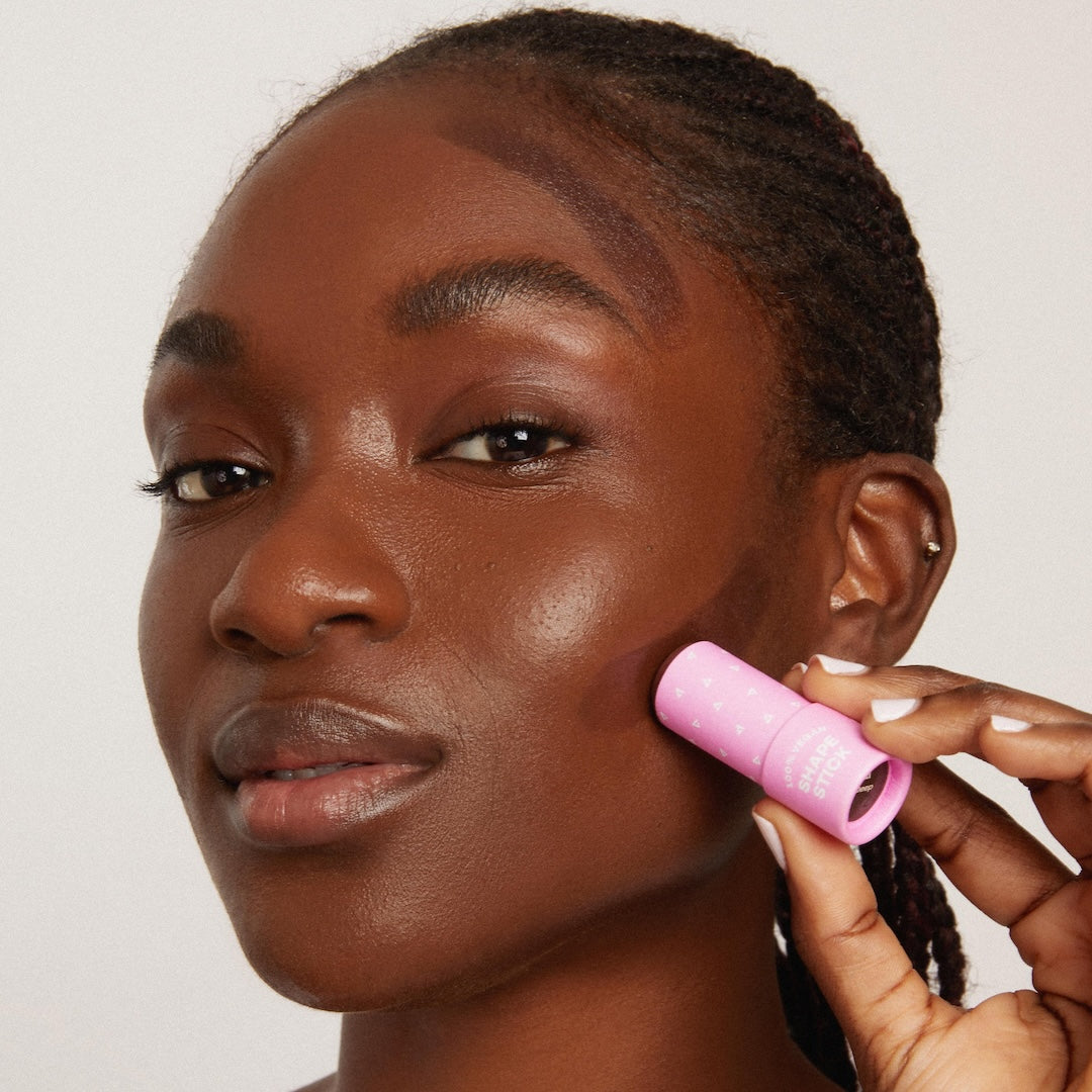 Woman using a cosmetic stick on her cheek against a plain background
