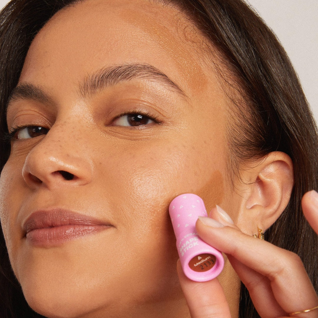 Woman applying makeup with a pink tube applicator to her face
