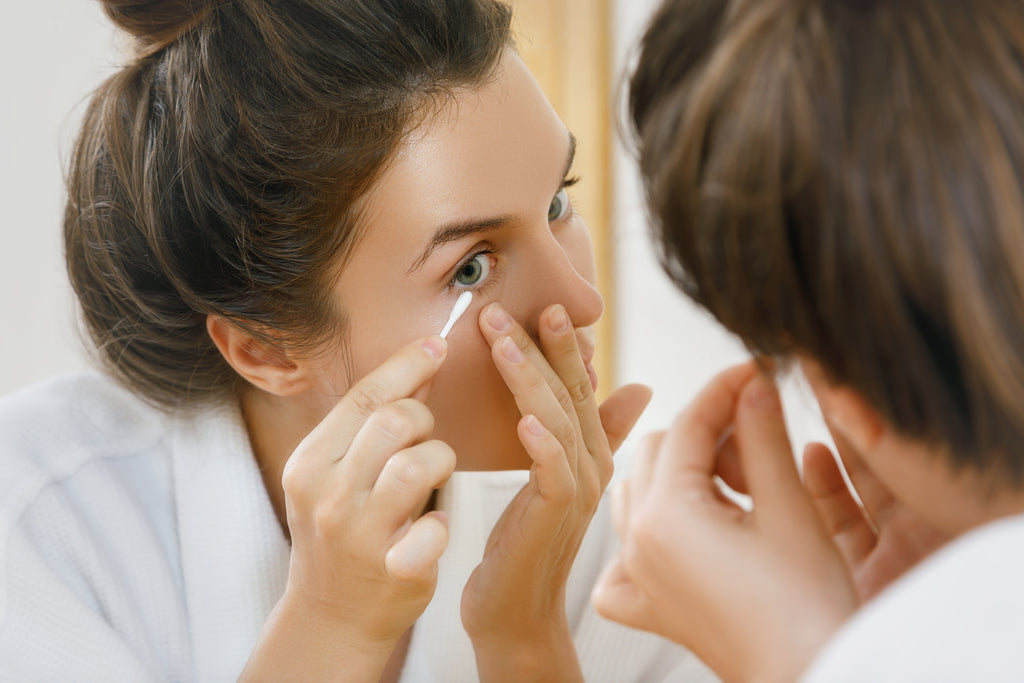 Woman applying makeup with a cotton bud in front of a mirror