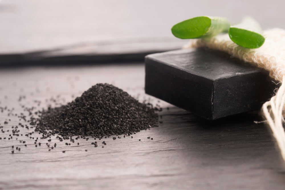 Bar of black charcoal soap with a pile of charcoal powder on a wooden surface.
