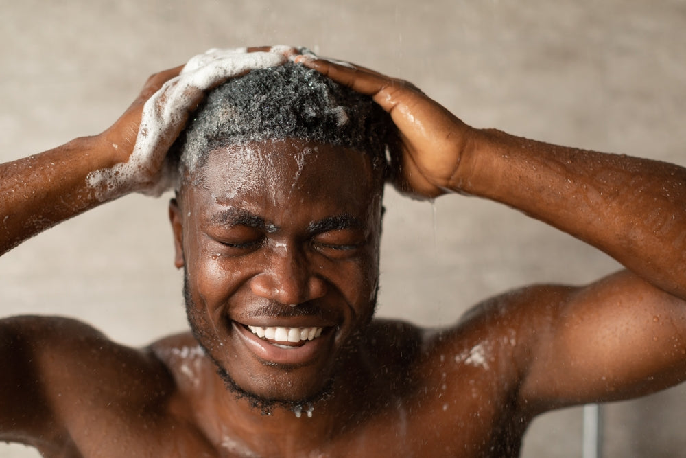 Man washing his hair with soap and water, smiling.