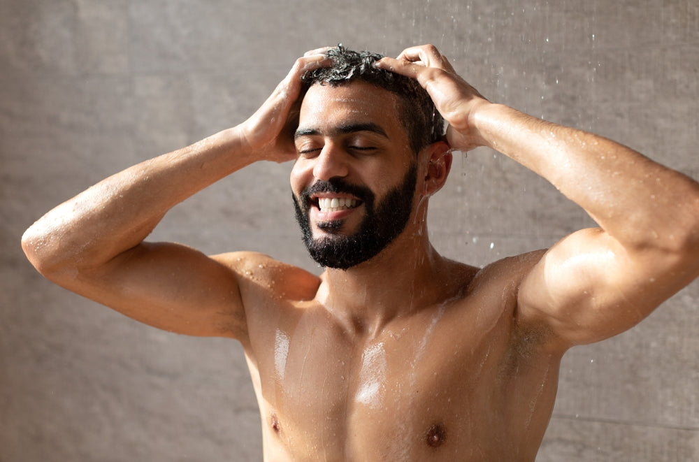 Man washing hair smiling in front of a neutral background