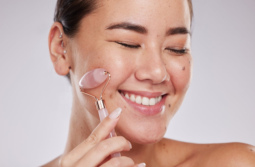 Woman using a rose quartz facial roller on her face against a gray background