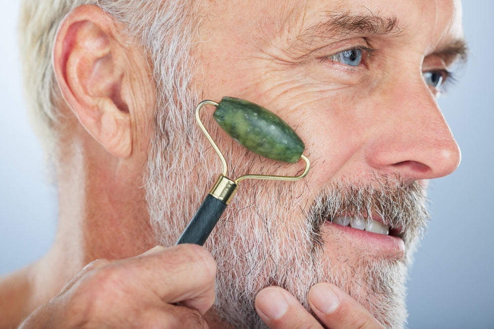 Man using a jade roller on his face against a light background