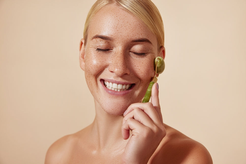 Woman using a jade roller on her face against a beige background