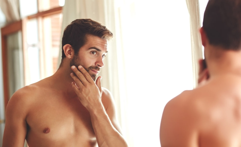 Man examining his reflection in a mirror, focusing on his beard.