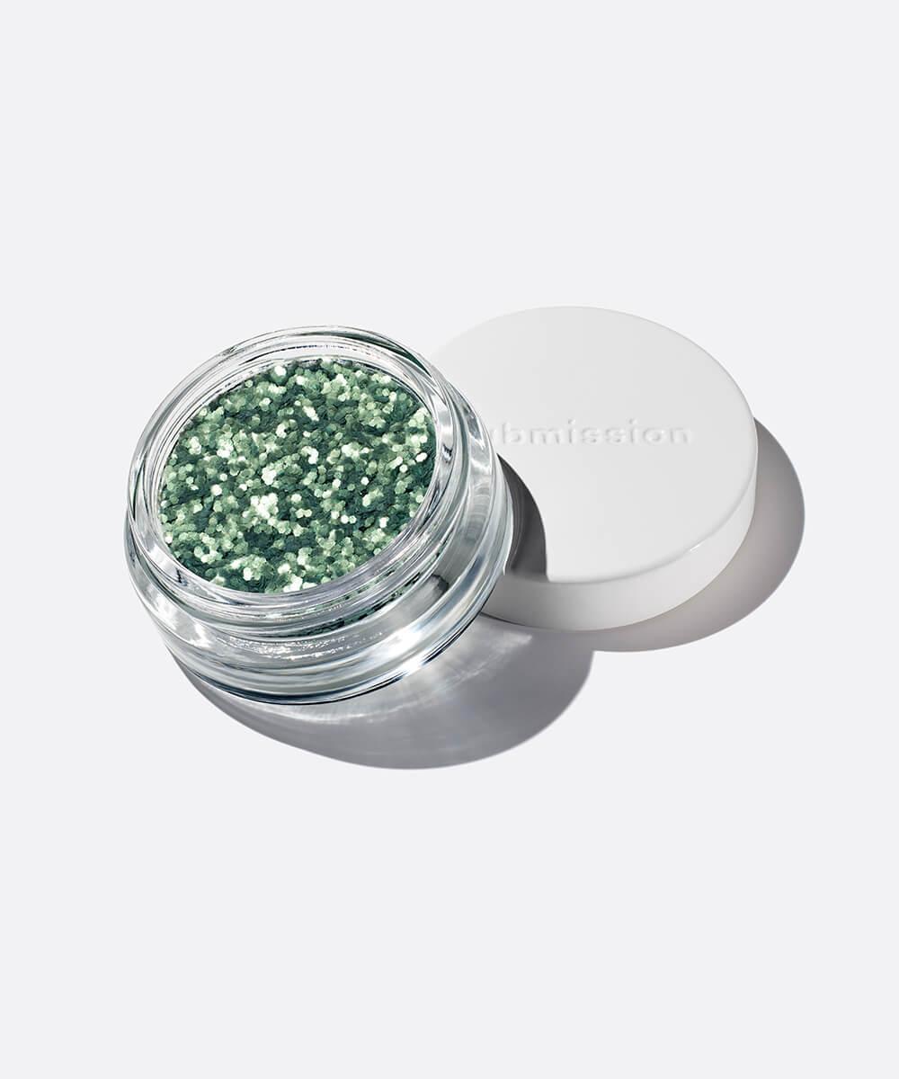 Open jar of green glitter with a white lid on a light gray background