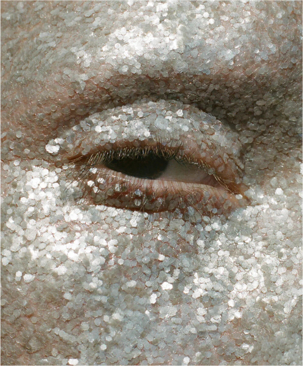 Close-up of a person's eye with silver glitter on the eyelashes and surrounding skin.